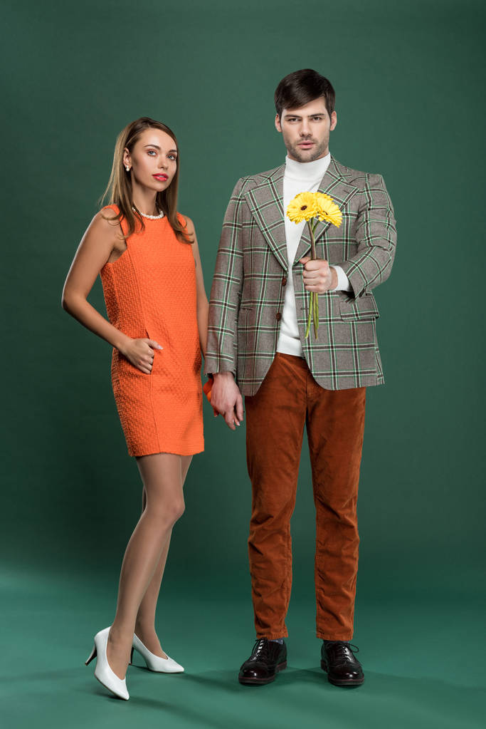 attraktives Paar in Vintage-Kleidung mit Blumen posiert auf grünem Hintergrund - Foto, Bild