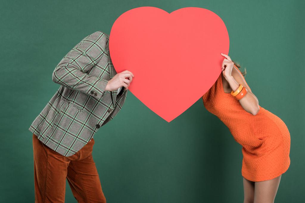 muž a žena pokrývající tváře se srdcem ve tvaru cedulkou izolované na zelené - Fotografie, Obrázek