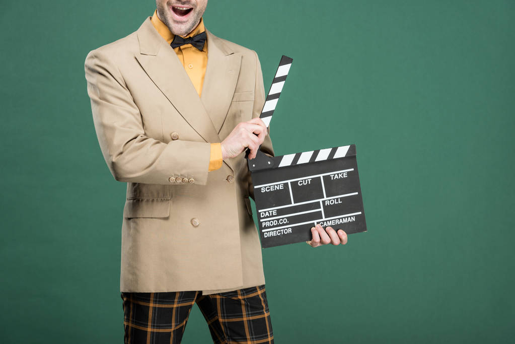 cropped view of excited man in vintage clothes holding film clapperboard isolated on green - Photo, Image