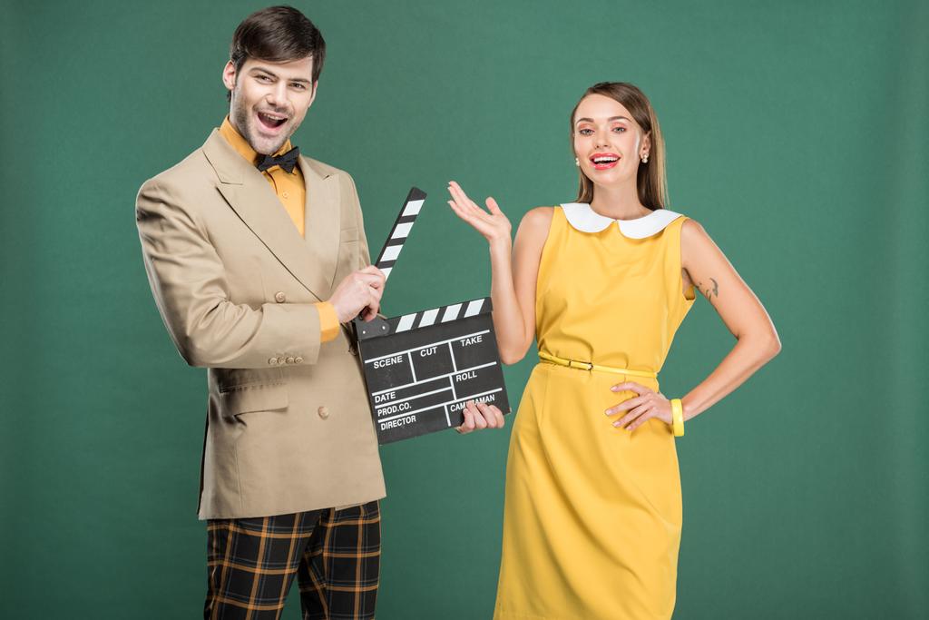 knappe man in vintage kleding bedrijf film Filmklapper terwijl mooie vrouw gebaren met hand geïsoleerd op groen - Foto, afbeelding