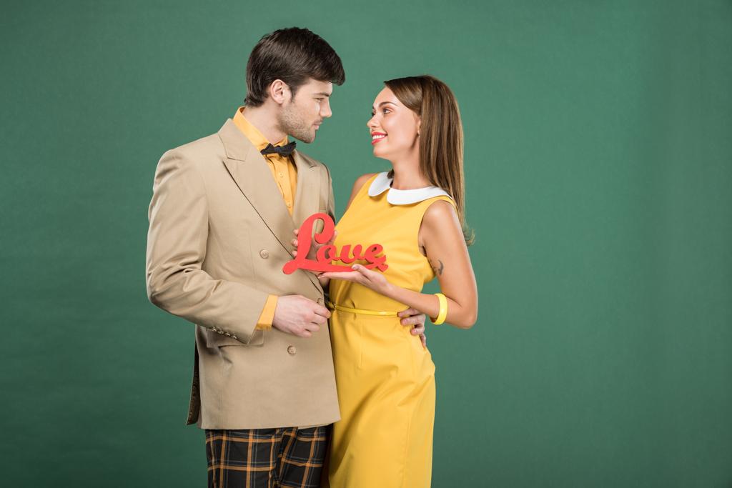 όμορφο ζευγάρι σε vintage ρούχα κρατώντας διακοσμητικά λέξη «αγάπη» που απομονώνονται σε πράσινο - Φωτογραφία, εικόνα
