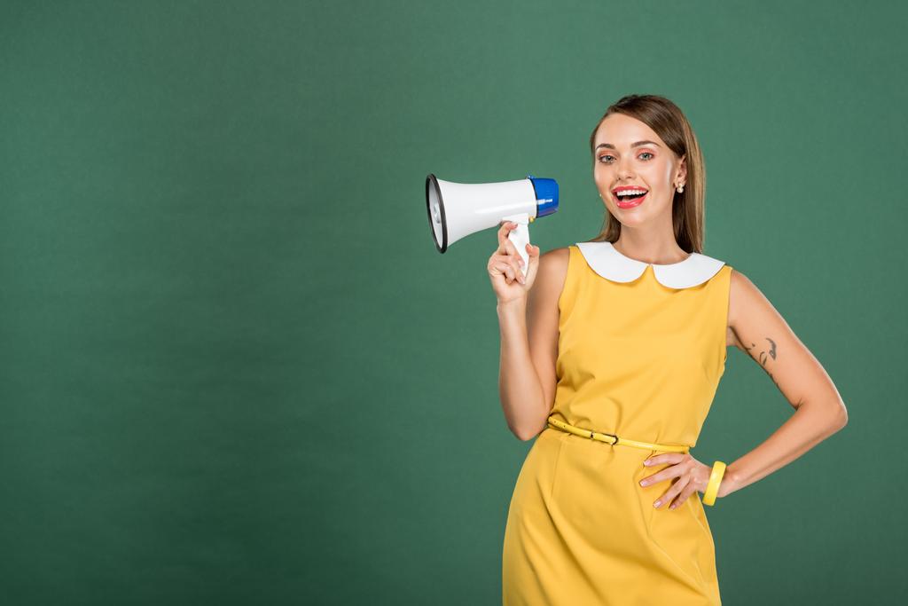 beautiful stylish woman in yellow dress shouting in loudspeaker isolated on green with copy space - Photo, Image