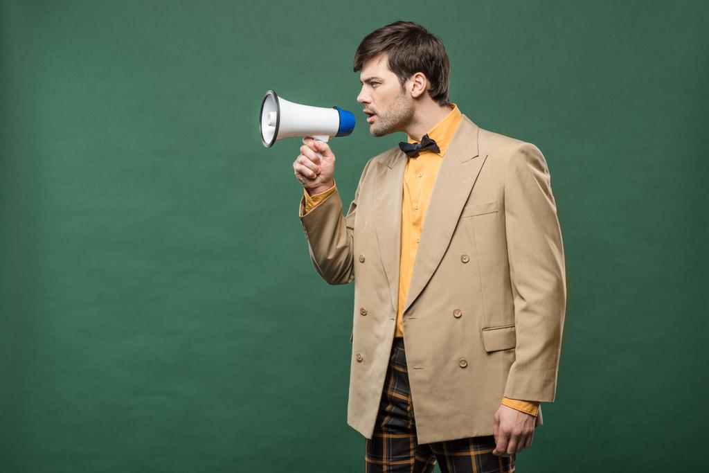 handsome man in vintage clothes talking in loudspeaker isolated on green with copy space - Photo, Image