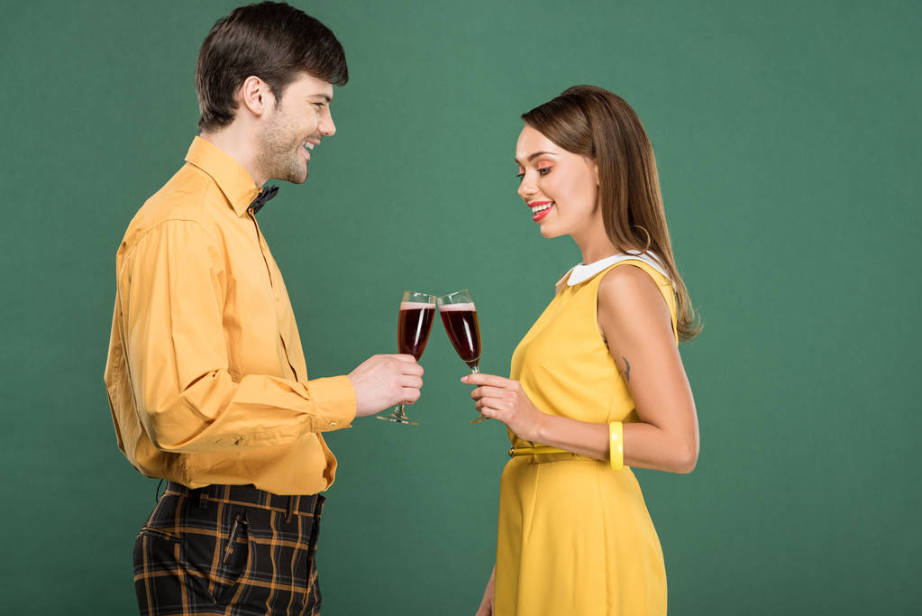 グリーンに分離された赤ワインのガラスをチリンとビンテージの服に美しい幸せなカップル - 写真・画像