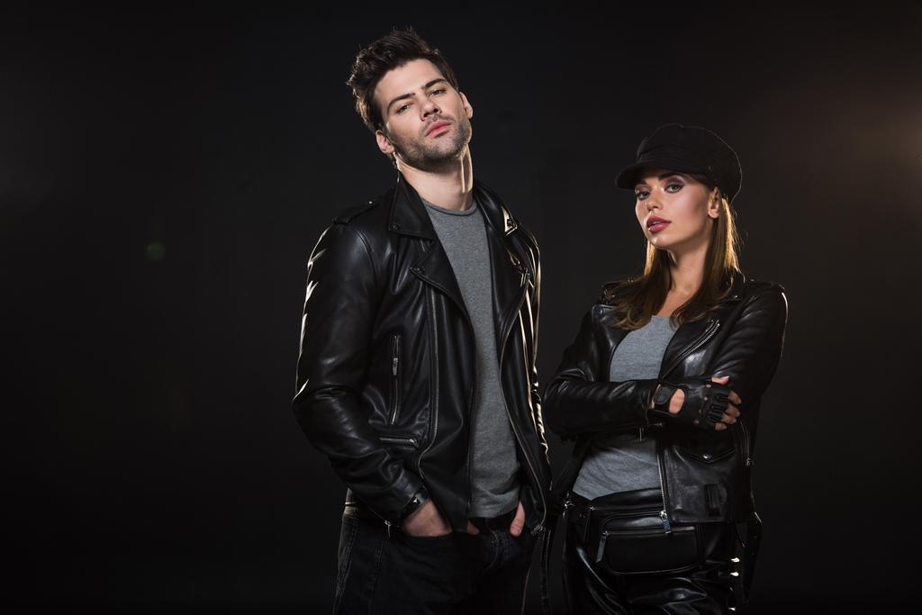 красивая пара в кожаных куртках, смотрящая в камеру и позируя на черном фоне
 - Фото, изображение