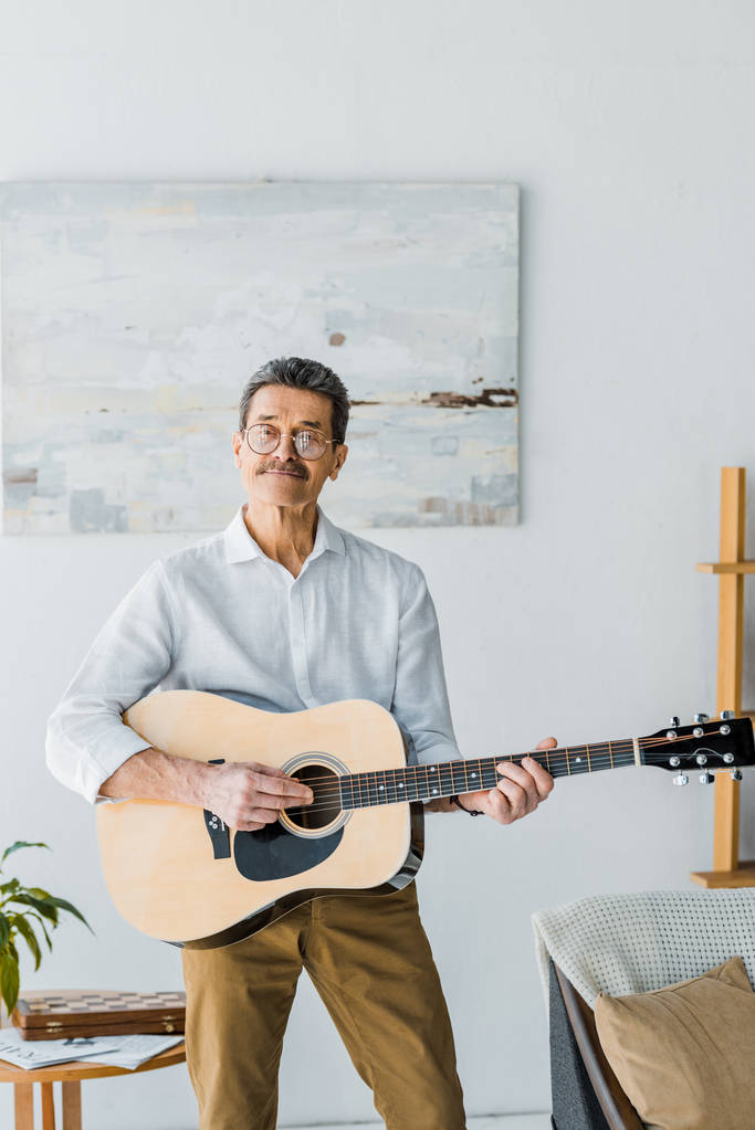 šťastný starší muž v brýlích hraje na akustickou kytaru doma - Fotografie, Obrázek