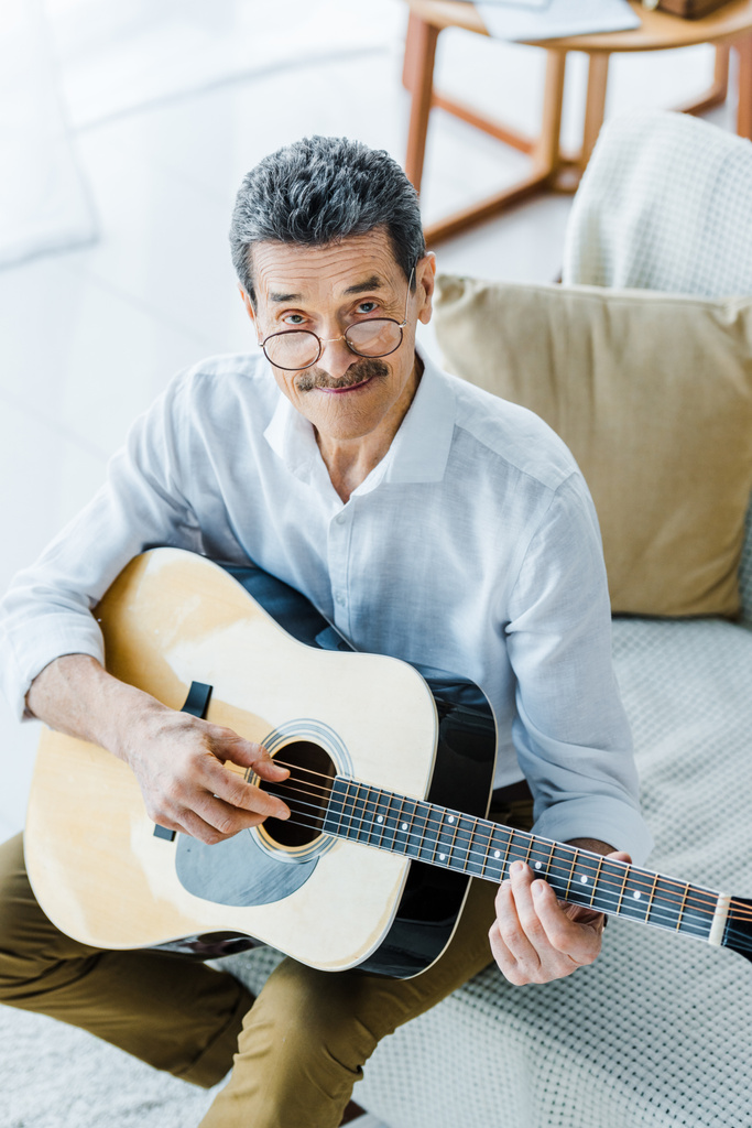 веселый пенсионер в очках играет на акустической гитаре дома
 - Фото, изображение