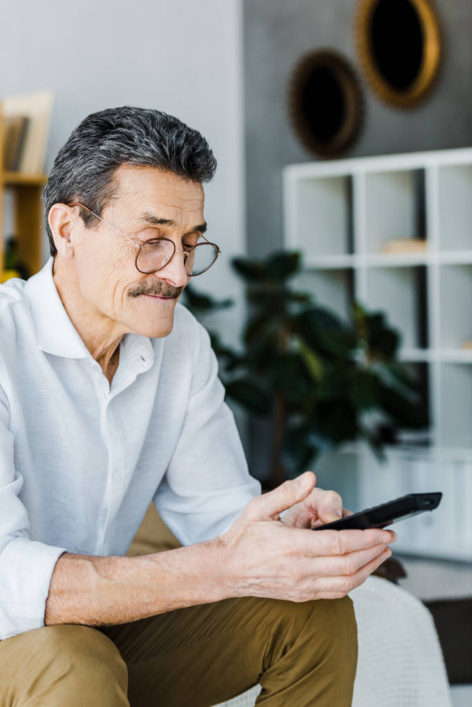 Senior man met snor kijken naar afstandsbediening in handen - Foto, afbeelding