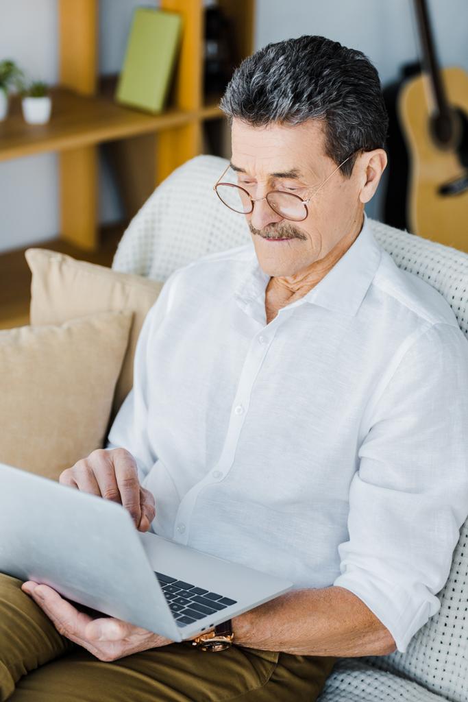 homme à la retraite dans des lunettes à l'aide d'un ordinateur portable assis sur le canapé
 - Photo, image