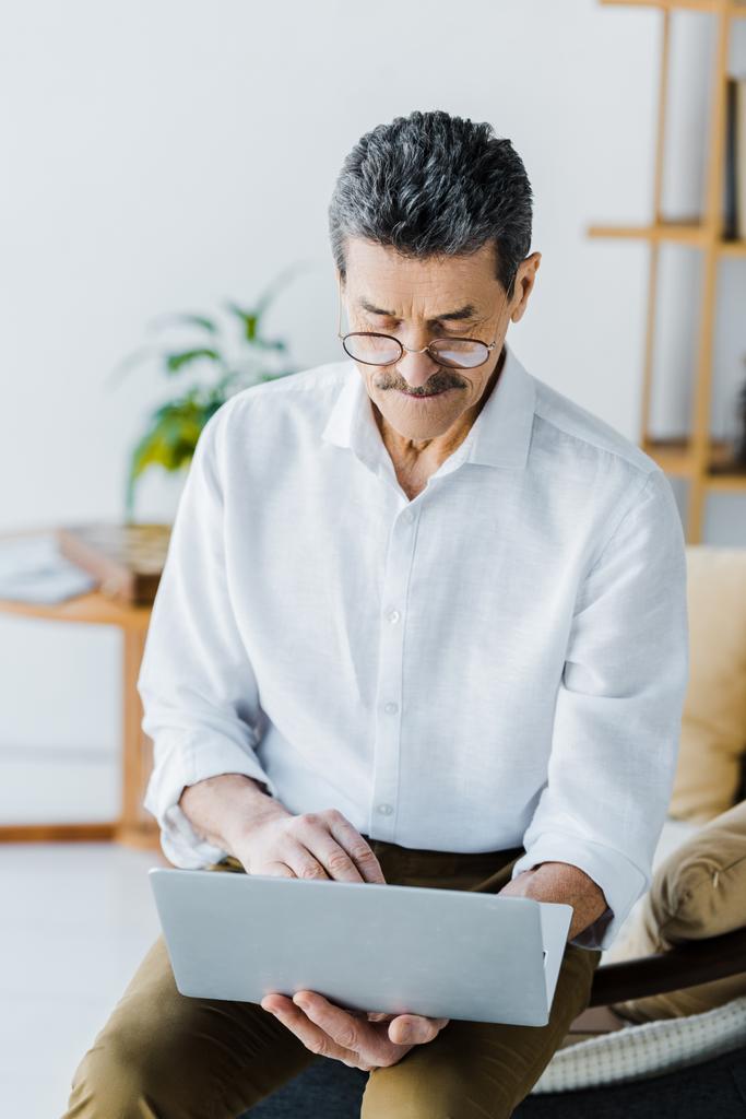 pensioner com bigode e óculos usando laptop enquanto sentado no sofá
 - Foto, Imagem