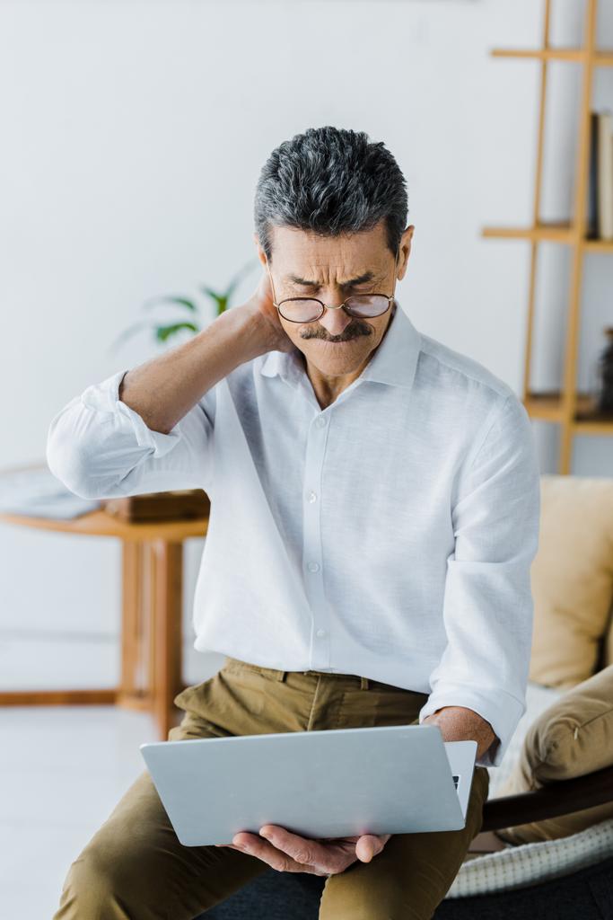 thoughtful pensioner with mustache looking at laptop at home - Photo, Image