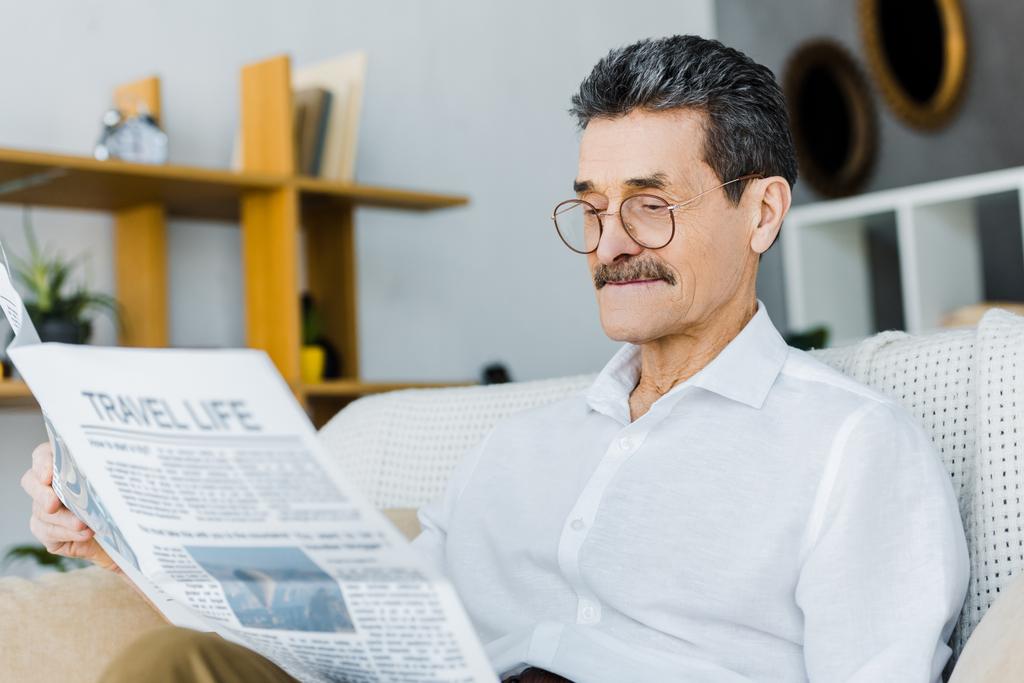 fröhlicher Senior mit Brille, der auf dem Sofa die Reisezeitung liest - Foto, Bild