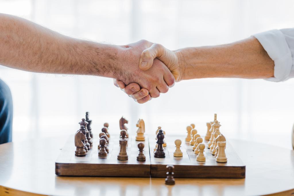 abgeschnittene Ansicht von Rentnern beim Händeschütteln nach dem Schachspielen zu Hause - Foto, Bild