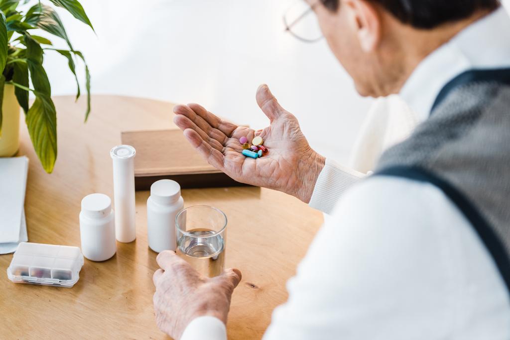 вибірковий фокус старшого чоловіка, дивлячись на таблетки, тримаючи склянку води
 - Фото, зображення