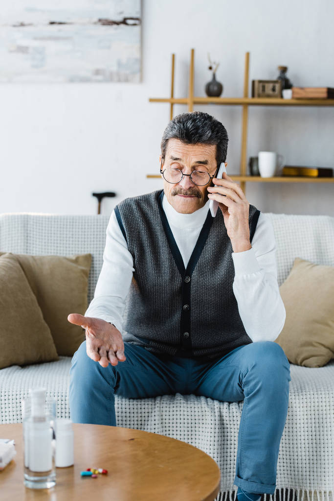 enfoque selectivo del hombre mayor hablando en el teléfono inteligente cerca de píldoras y un vaso de agua
 - Foto, Imagen