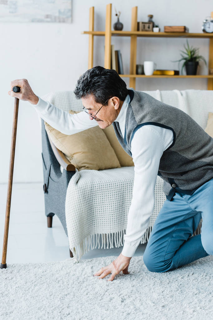 senior man in glasses holding walking cane while trying standing up at home - Photo, Image