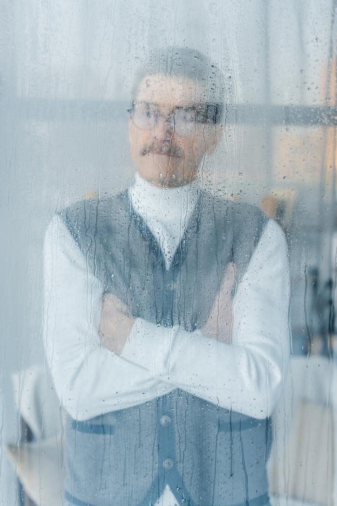 zamyšlený bývalý muž, který stojí s překřížením rukou okna  - Fotografie, Obrázek