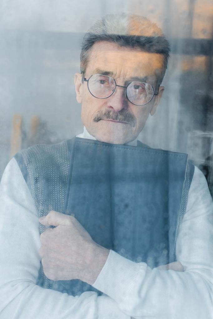 грустный пожилой мужчина обнимает фотоальбом у окна
  - Фото, изображение