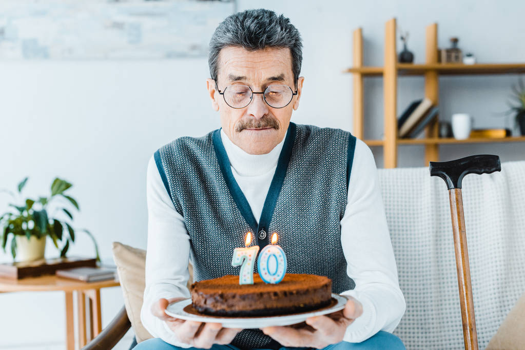 triste homme âgé tenant gâteau d'anniversaire tout en étant assis sur le canapé un dans le salon
  - Photo, image