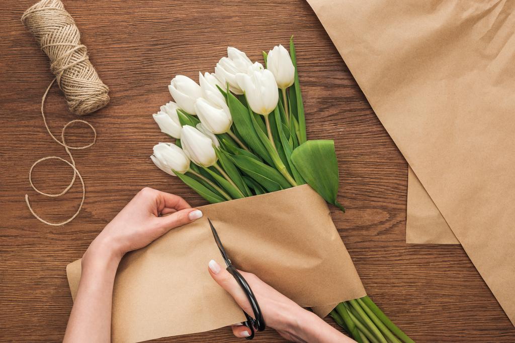 vista parcial de en floristería corte de papel artesanal mientras se hace ramo de primavera sobre fondo de madera
 - Foto, Imagen