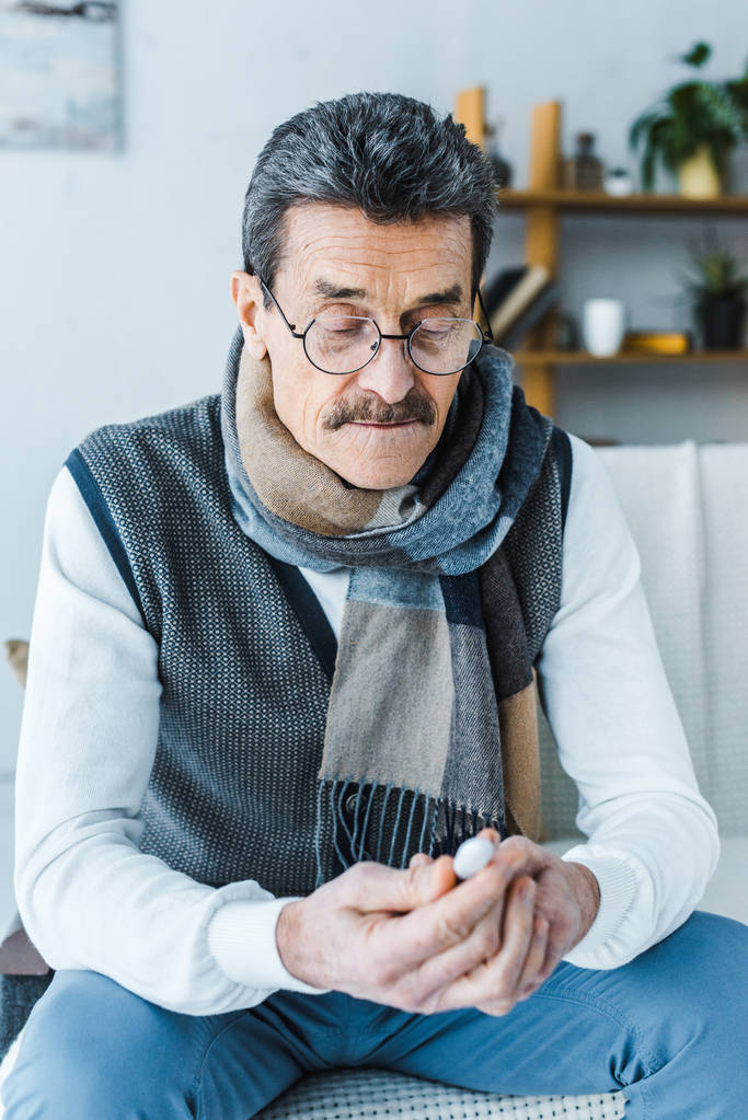 больной пожилой человек в шарфе смотрит на термометр дома
 - Фото, изображение