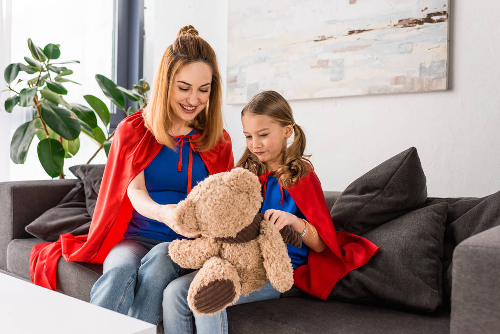 Lächelnde Mutter und Kind in roten Mänteln mit Teddybär  - Foto, Bild