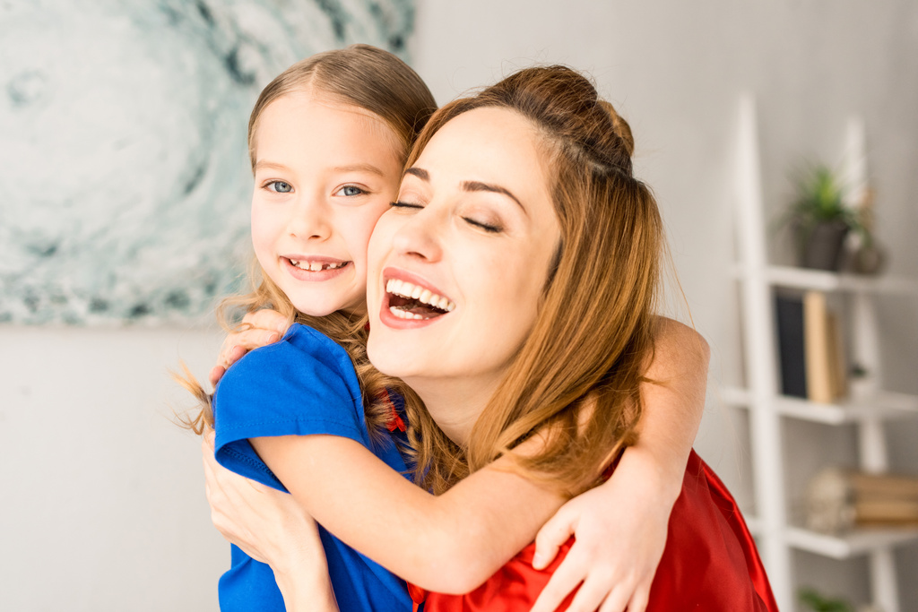 Χαμογελώντας η μητέρα και παιδί σε κόκκινο μανδύες στο σπίτι σε κοντινό πλάνο - Φωτογραφία, εικόνα