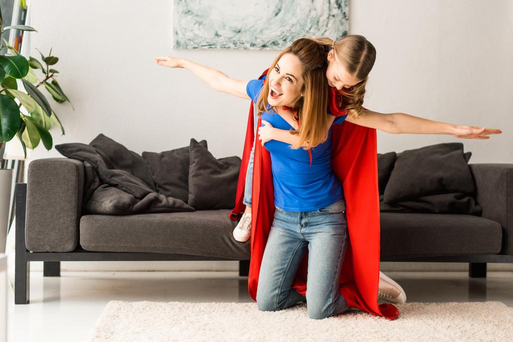 hija y madre en capas rojas abrazándose y jugando en casa
 - Foto, imagen