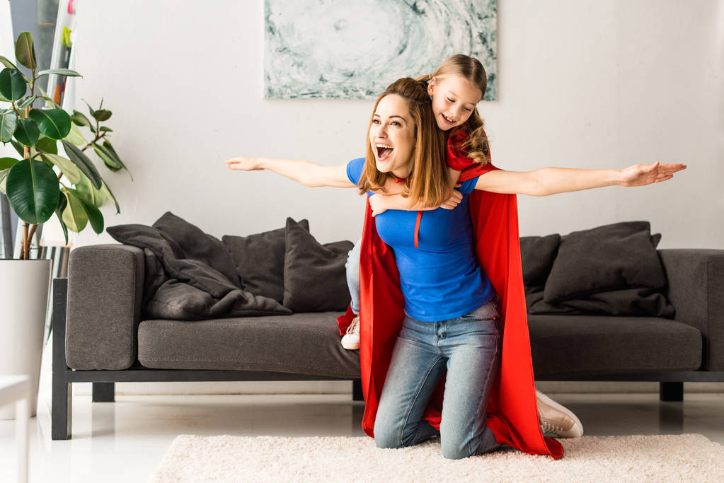 hija y madre en capas rojas sonriendo y jugando en casa
 - Foto, Imagen