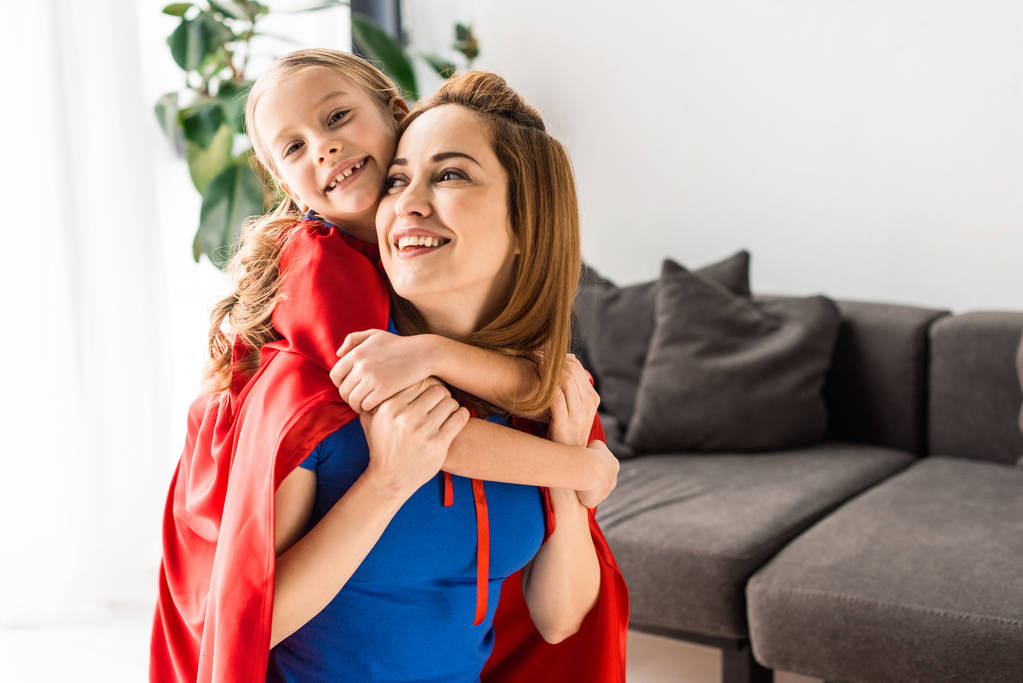daughter and mother in red cloaks hugging and smiling at home  - Photo, Image