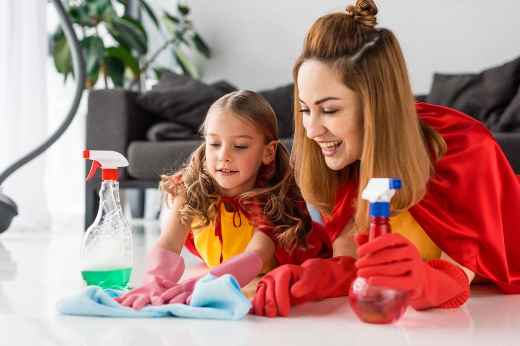 matka i dziecko w czerwone pelerynki i gumowe rękawiczki z spraye mycie podłogi - Zdjęcie, obraz