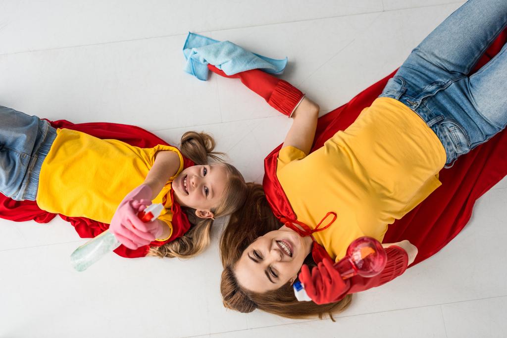 Draufsicht von Mutter und Kind in roten Umhängen und Gummihandschuhen mit Sprays und Teppich - Foto, Bild