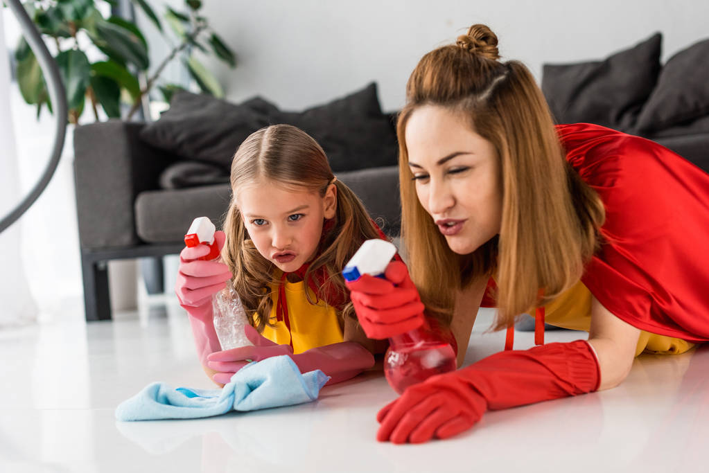 moeder en dochter in rode capes en rubberen handschoenen wassen vloer thuis - Foto, afbeelding