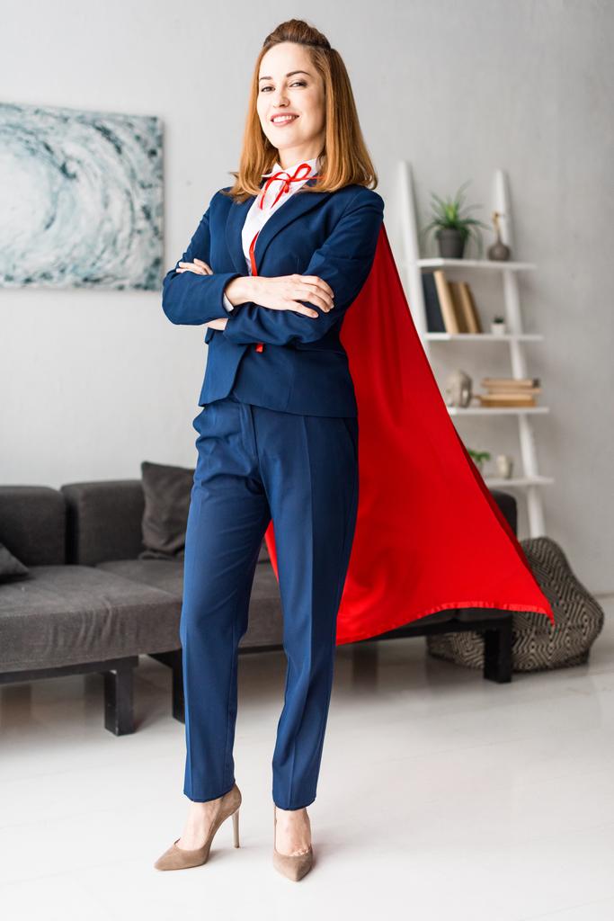 Lächelnde Geschäftsfrau in blauem Anzug und rotem Umhang blickt in die Kamera - Foto, Bild