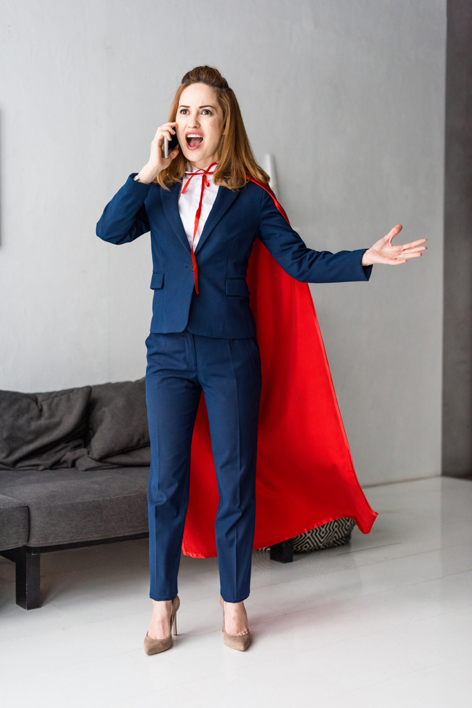 Screaming businesswoman in blue suit and red cape talking on smartphone - Photo, Image