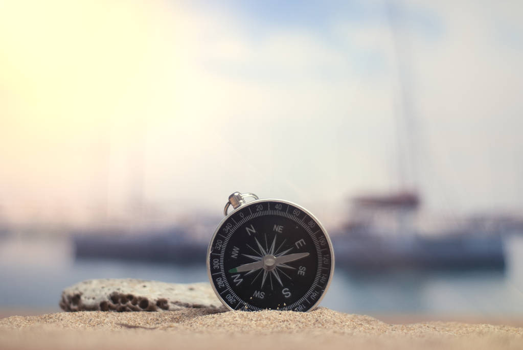 Zeit zu reisen. eine Idee für den Tourismus mit einem Kompass im Sand mit Korallen im Hintergrund des Meeres und einem Parkplatz für Yachten - Foto, Bild