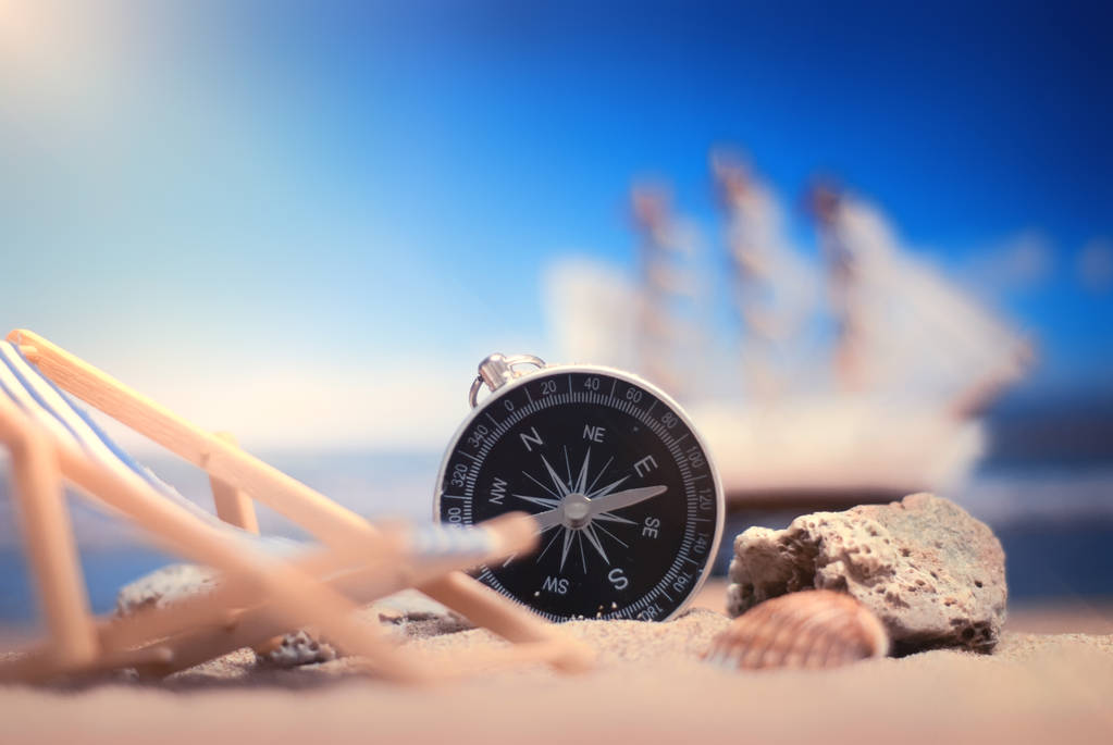Tijd om te reizen. Idee voor toerisme met kompas en chaise lounge op het zand met koralen op de achtergrond van de zee en het schip - Foto, afbeelding