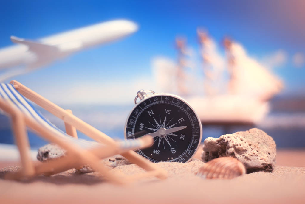 Tijd om te reizen. Idee voor toerisme met kompas en chaise lounge op het zand met koralen op de achtergrond van de zee, schip en vliegtuig - Foto, afbeelding