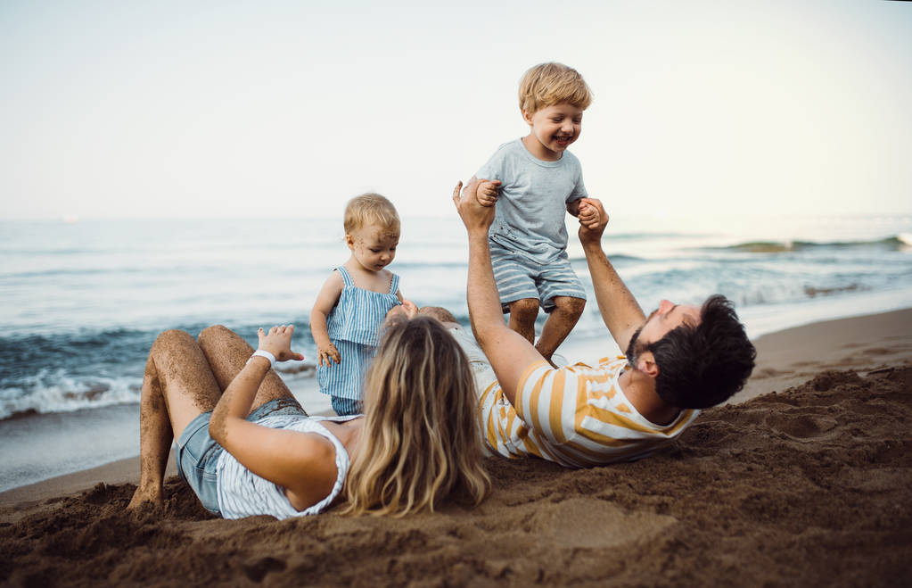 Una familia con dos niños pequeños tumbados en la playa de arena en las vacaciones de verano
. - Foto, imagen
