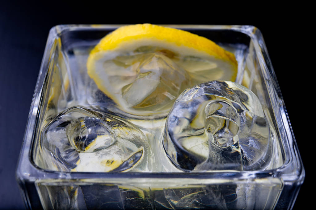 Koude drank in een glas op de keukentafel. Citroen en ijs met water de beste manier om af te koelen op een zomerdag. Donkere achtergrond. - Foto, afbeelding