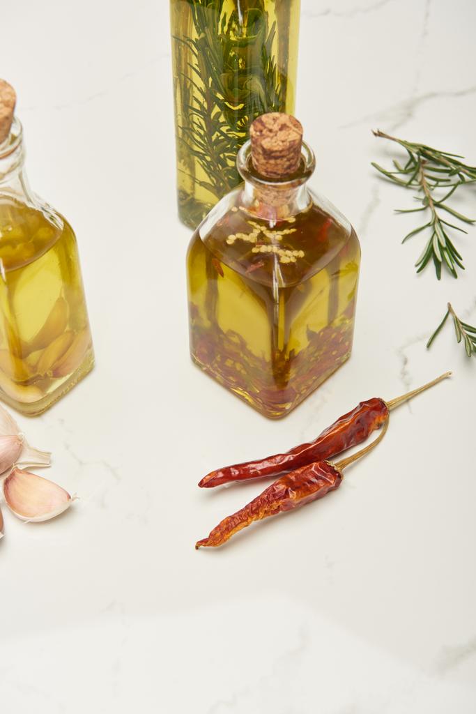 botellas de aceite de corcho aromatizado con romero y diferentes especias en la superficie blanca
 - Foto, Imagen