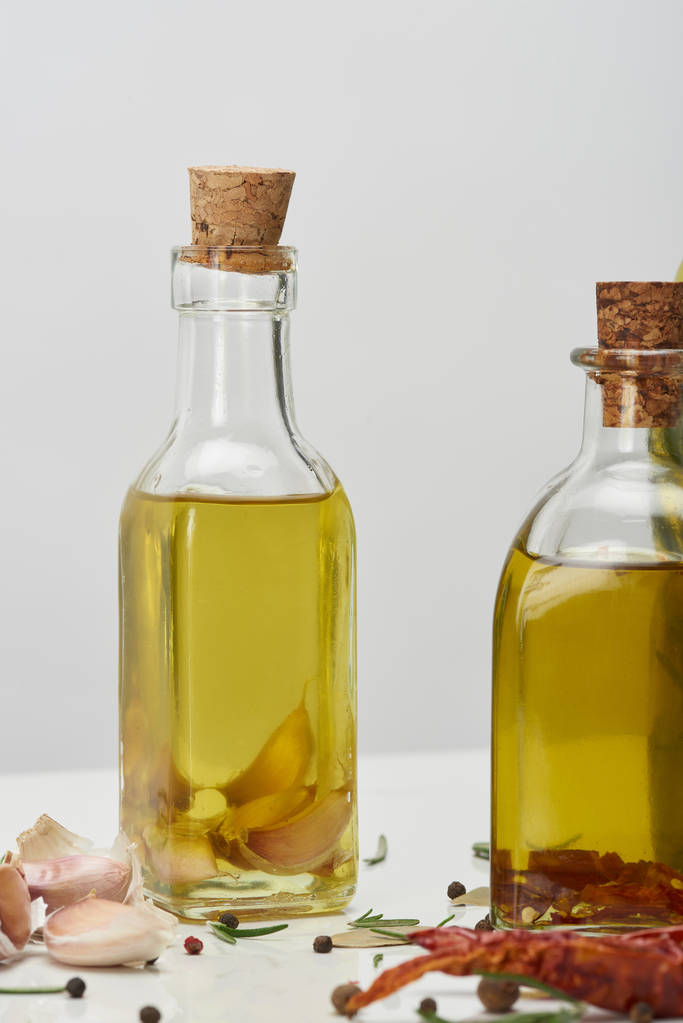 varias botellas de aceite aromatizado con diferentes especias y romero en la superficie blanca
 - Foto, Imagen