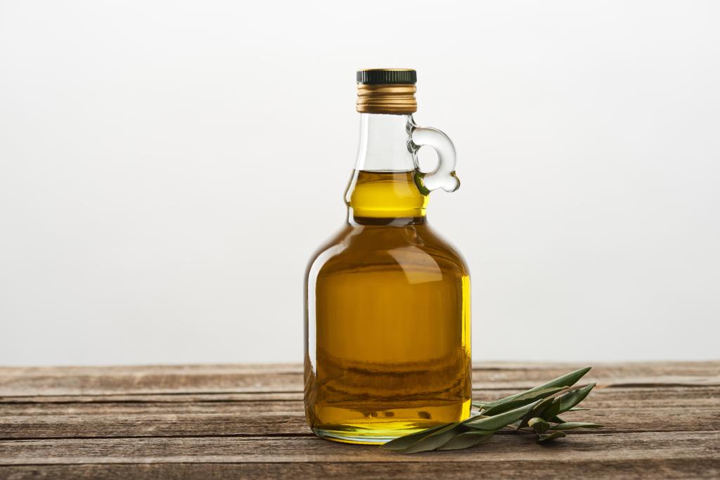 бутылка оливкового масла и листья оливкового дерева, изолированные на сером
  - Фото, изображение