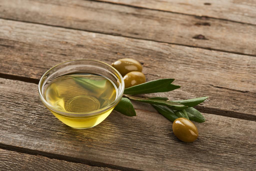 стеклянная чаша с маслом, оливковыми листьями и оливками на коричневой деревянной поверхности
 - Фото, изображение