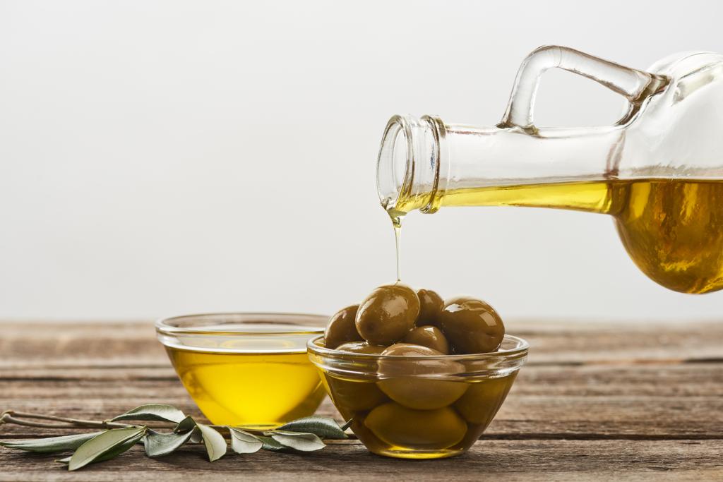 verter en un tazón de vidrio con aceitunas, un tazón lleno de aceite y una rama de olivo sobre una superficie de madera
 - Foto, imagen