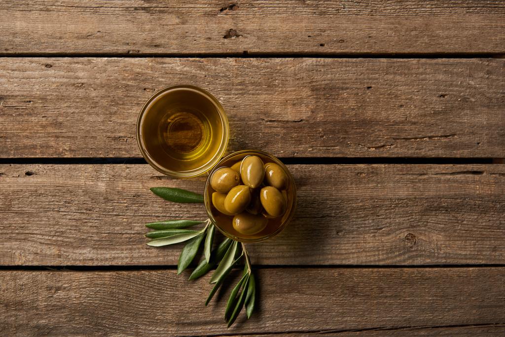Blick von oben auf Glasschalen mit Oliven und Öl und Olivenzweig auf Holzoberfläche - Foto, Bild