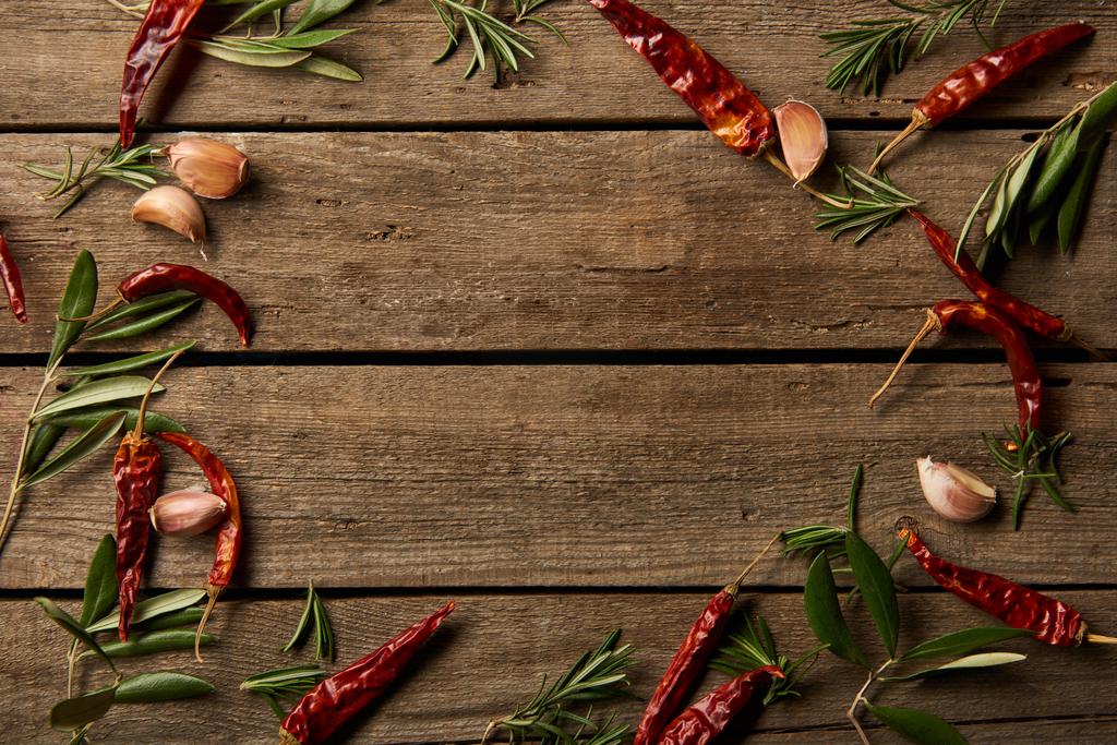 top view of red hot chili peppers, rosemary branches and garlic cloves on wooden background - Photo, Image