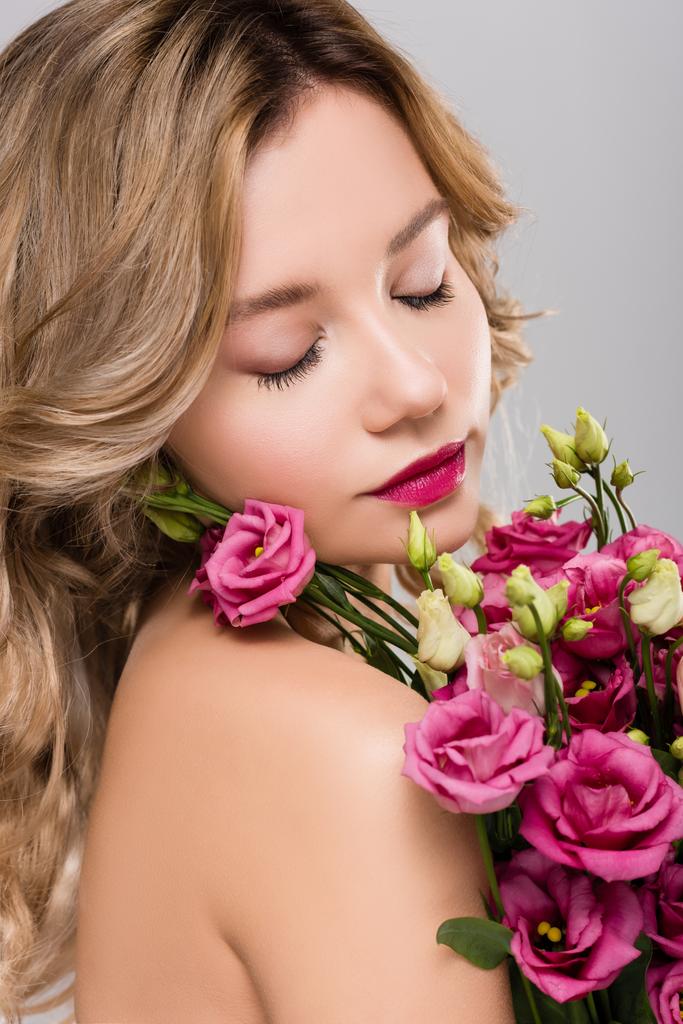 обнаженная красивая блондинка с закрытыми глазами, позирующая с весенним цветочным букетом Юстомы, изолированным на сером
 - Фото, изображение