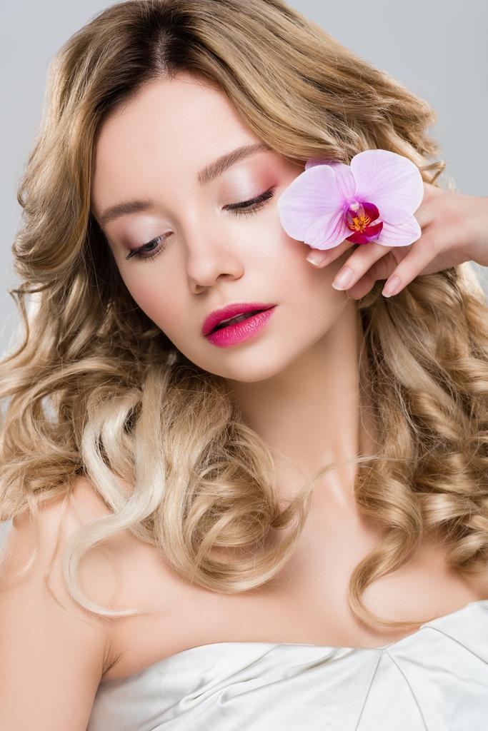 young woman holding purple orchid near face isolated on grey - Photo, Image