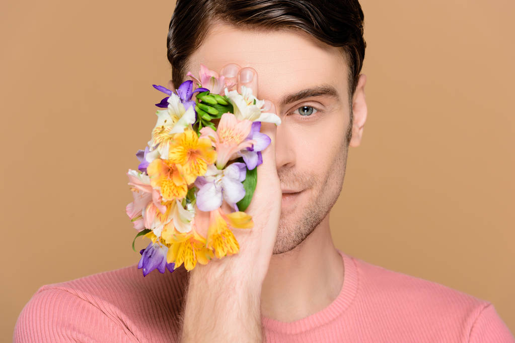 Χαμογελαστός άνθρωπος που καλύπτει ένα μάτι με λουλούδια Αλστρομέριες αφενός απομονώνονται σε μπεζ - Φωτογραφία, εικόνα